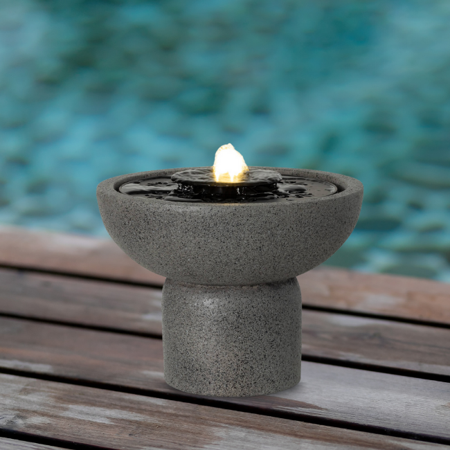 A stylish and modern outdoor water feature sitting on a wooden deck beside a swimming pool, adding a serene touch.